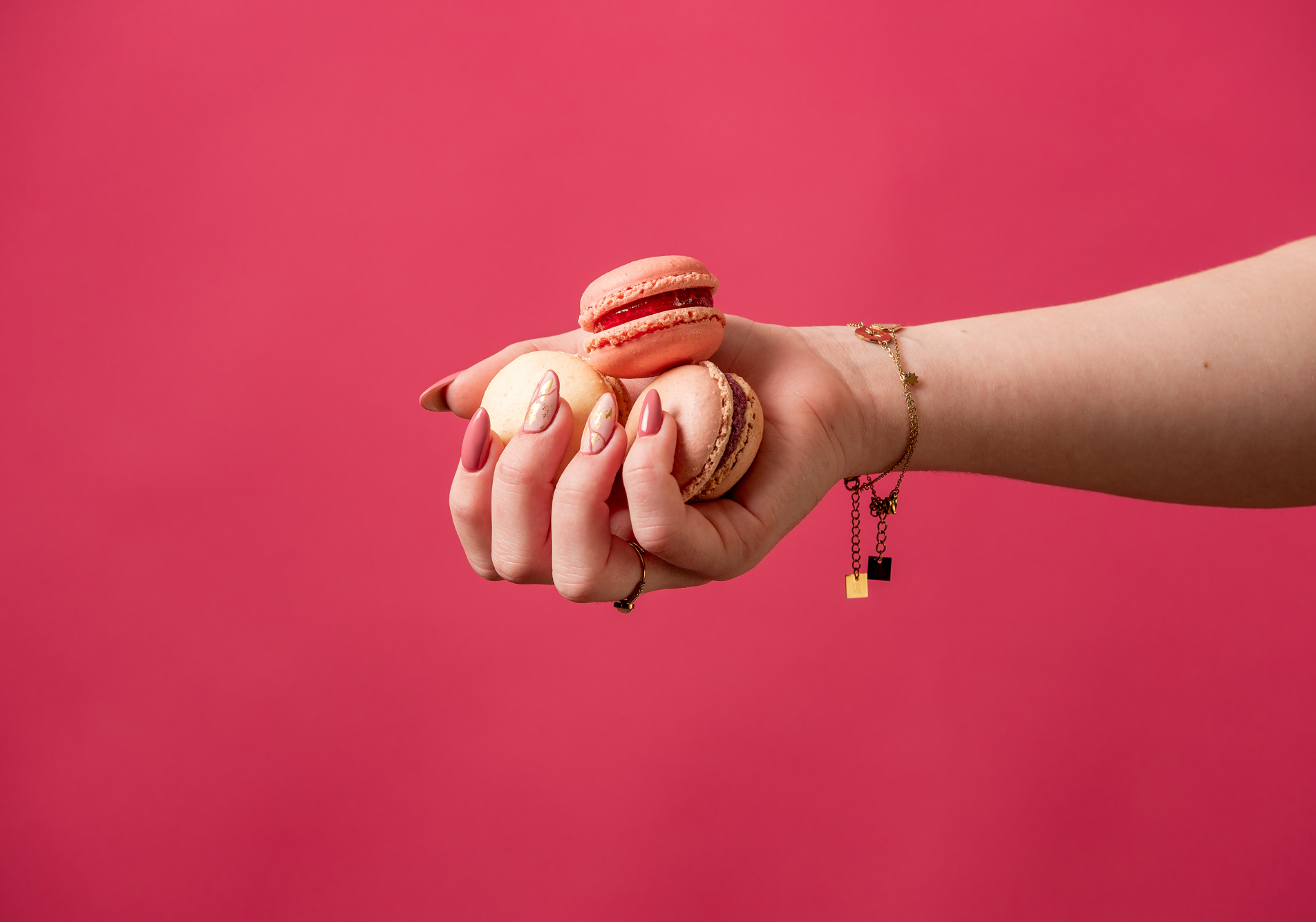 Réalisation d'une affiche publicitaire photo mettant en scène une main tenant des macaron avec une belle manucure sur un fond rose.